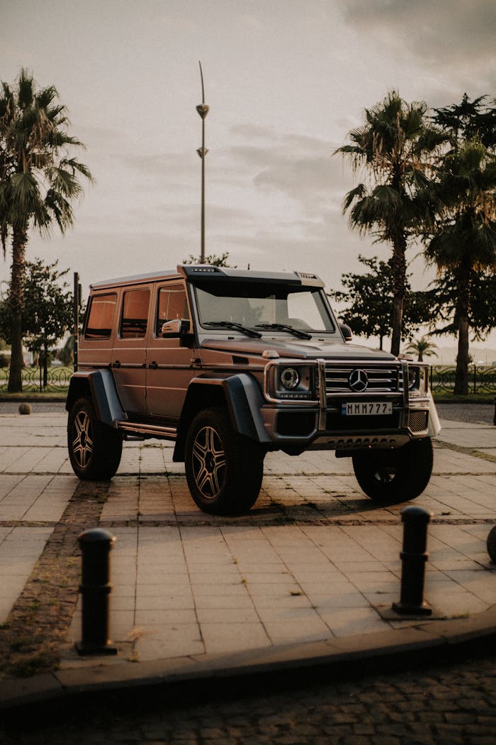 Parked Mercedes-Benz G-Class SUV on Batumi street with palm trees at sunset.